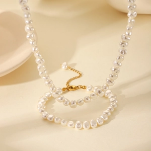 Elegant French baroque irregular pearl necklace with gold clasp on beige surface
