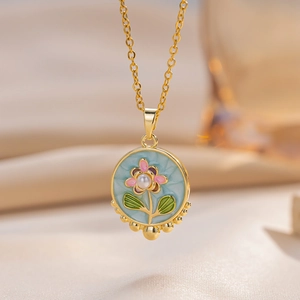 Golden necklace with blue enamel floral pendant and pearl center on warm silk fabric