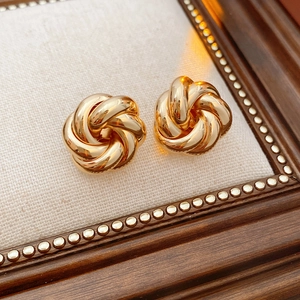Macro shot of gold-plated twisted flower earrings on beige fabric with vintage frame