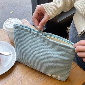 Close-up of a blue corduroy makeup bag being unzipped on a wooden cafe table