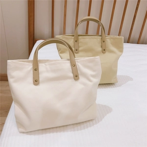 Close-up of canvas tote bag with brown leather handles and reinforced metal rivets