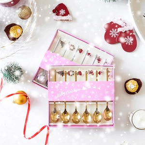 Macro shot of a 6-piece golden Christmas spoon set with festive charms in a pink gift box