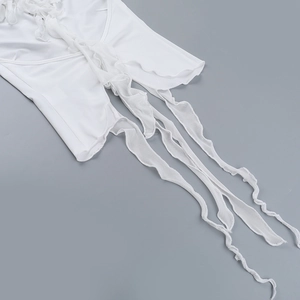 Detail shot of white top featuring delicate ruffles and long fabric fringe tassels