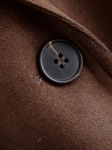 Detailed macro view of dark brown suede coat fabric with a stylish black resin button