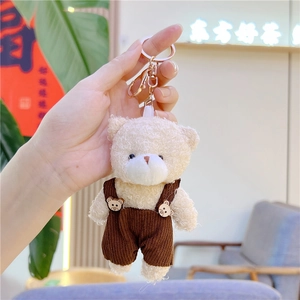 Primer plano de llavero de oso de peluche crema con peto de pana marrón y gancho metal