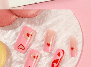 Detail view of pink French press-on nails with red heart patterns on marble stand