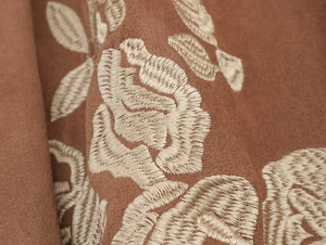Close-up detail of floral embroidery on premium brown suede fabric with rich texture