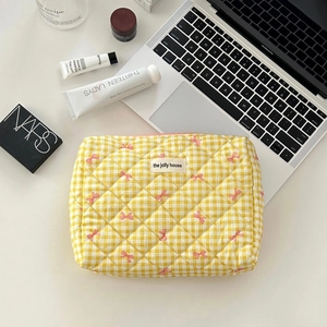 Detailed close-up of yellow checkered makeup bag with quilted texture and pink bows