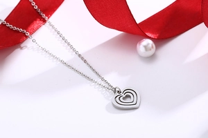 Silver layered heart necklace on white surface with red ribbon and pearl detail