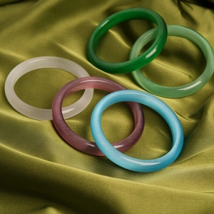 Macro detail of cat eye stone bangles in five colors on elegant green silk fabric