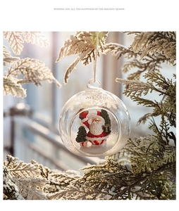 Close-up of clear Christmas ball with Santa Claus and tree hanging on snowy pine branch