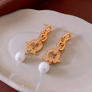 Close-up of gold chain earrings with horseshoe motif, pavé stones, and white pearl