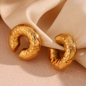 Dettaglio macro di orecchini placcati oro 18K con finitura martellata su seta beige