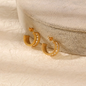 Detail of gold C-shaped earrings with woven texture and clear zircon stones on velvet