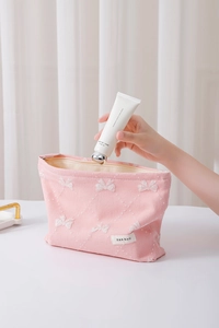 Dettaglio che mostra una mano che mette la crema nel beauty case rosa con fiocchi