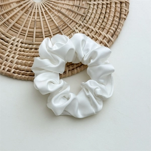 Detail of white satin scrunchie with silky texture and folds on a woven rattan mat