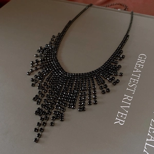 Close-up of elegant black tassel bib necklace with rhinestone fringe on a gray background