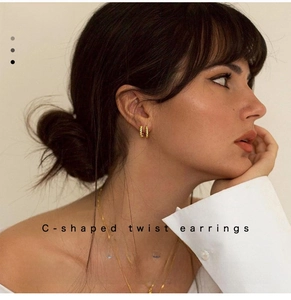 Close-up of a model wearing golden C-shaped twisted hoop earrings with a textured finish