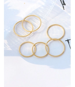 Detailed view of six minimalist golden rings made of polished stainless steel on white surface