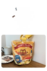 Detail view of yellow canvas bucket bag with Happy Pilot cartoon cat print and sturdy strap