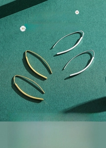 Close-up of minimalist gold and silver U-shaped hook earrings on green background