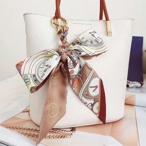 Detail of floral silk scarf bow pendant on a white leather handbag with gold hardware