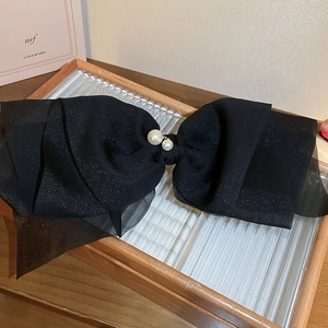 Détail d'une grande pince à cheveux nœud noir scintillant avec perles sur bois verni