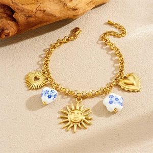 Golden chain bracelet with sun heart pendants and blue floral ceramic beads on wood