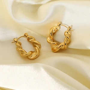 Close-up of twisted gold-plated stainless steel hoop earrings on white satin fabric