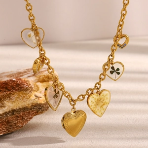 Dettaglio dei ciondoli a cuore e quadrifoglio placcati oro 18K su una base di pietra