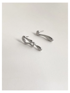 Detailed macro view of asymmetric silver liquid metal stud earrings on white paper
