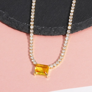 Detailed shot of gold necklace featuring yellow square gemstone and clear zircon accents