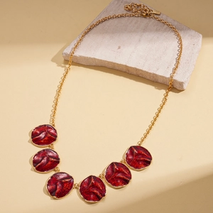 Close-up of golden necklace with six red enamel round charms featuring unique pleated texture