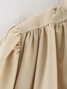 Detail showing elegant ruched shoulders and fine woven texture of the beige jacket