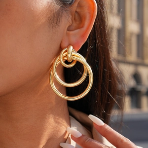 Macro close-up of triple interlocking gold hoop earrings worn by a model in natural light