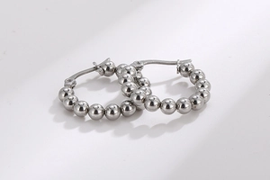 Close-up of silver steel beaded hoop earrings with smooth metallic spherical texture