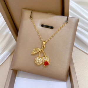 Detailed shot of golden cherry pendant with red heart gemstone in beige jewelry box