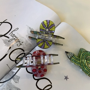 Three acrylic claw clips in colorful patterns on a stylish magazine background