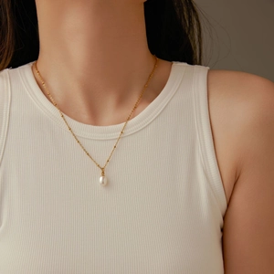 Élégant collier doré avec un pendentif en perle goutte porté sur le cou d'une femme