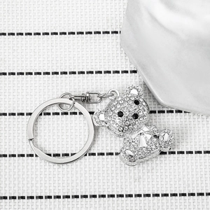 Sparkling crystal bear keychain with silver metal ring and chain on a white textured background