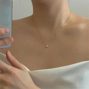 Close-up of minimalist gold chain necklace with a single white zircon pendant worn by person