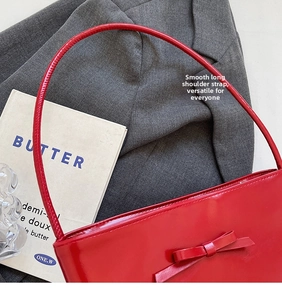 Detail of red patent leather shoulder bag featuring a stylish bow and slim strap design