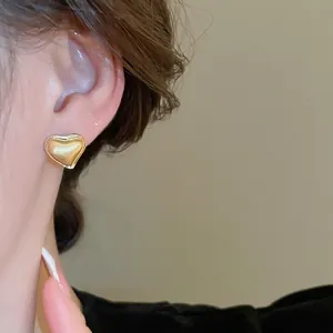 Elegant gold plated heart earrings with brushed metal finish on model's ear