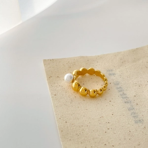 Detailed view of a gold beaded twist ring featuring a single white pearl on linen fabric