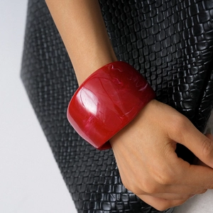 Macro detail of red resin bangle with marble texture worn against a black bag