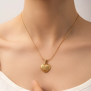 Close-up of gold heart pendant necklace with matte brushed texture on a female model