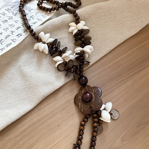 Detail of bohemian necklace featuring dark wood beads, white cowrie shells and carved flower