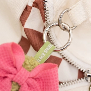 Detail of brown checkerboard canvas bag with green label and pink bow accessory