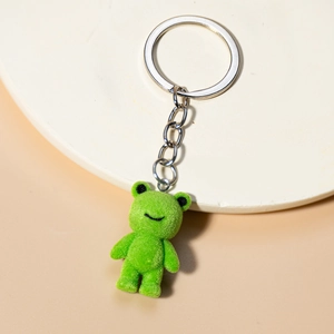 Detail of cute green flocked frog plush keychain with silver metal ring on a tray