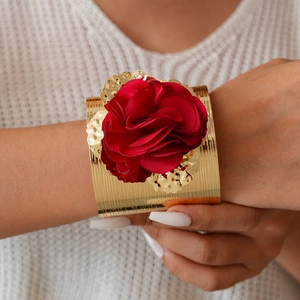 Detail of a wide gold metal cuff bracelet with a large 3D red fabric rose and gold leaves